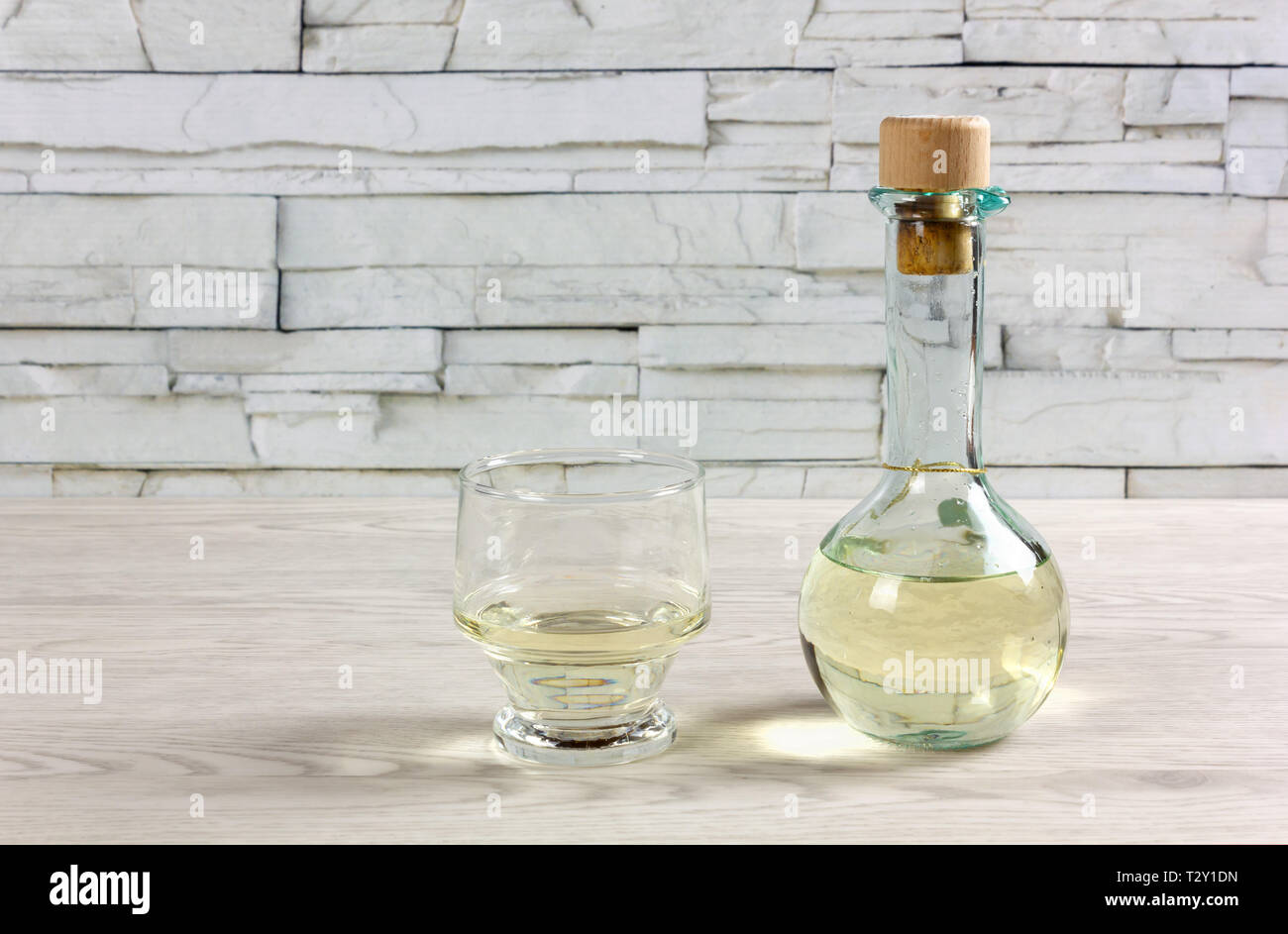 Eine kleine Flasche auf einen hölzernen Tisch, mit einem Korken verschlossen, voller Weißwein und neben einem Glas Stockfoto