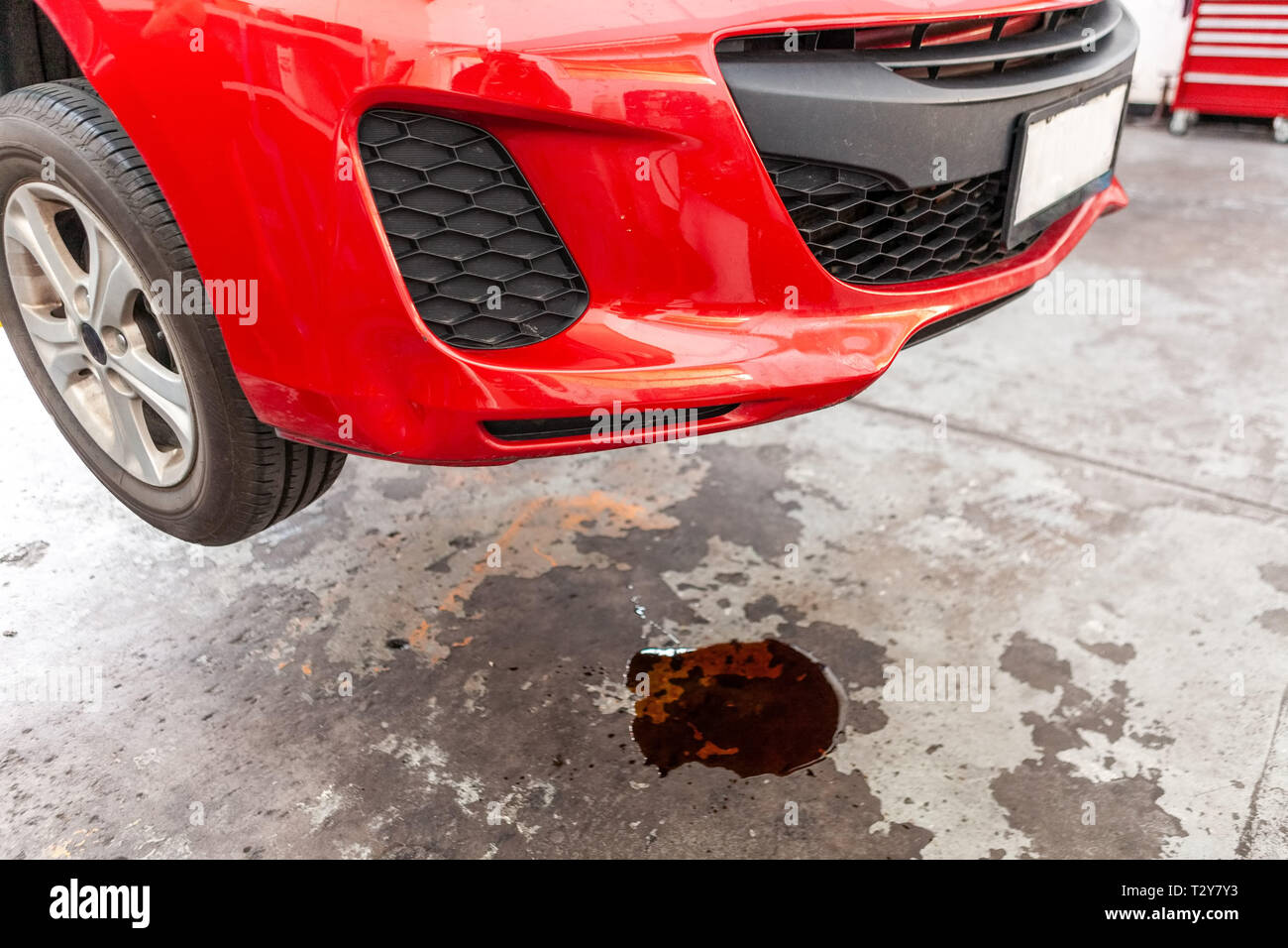 Konzept der Auto ölleck dargestellt mit roten Fahrzeug und Pfütze von Öl unter Stockfoto