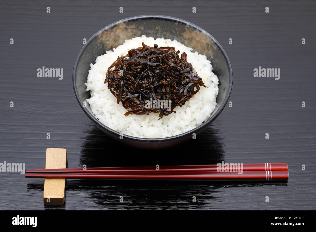 Japanisches Essen, Tsukudani der konbu auf gekochten Reis weiß auf schwarzem Hintergrund Stockfoto