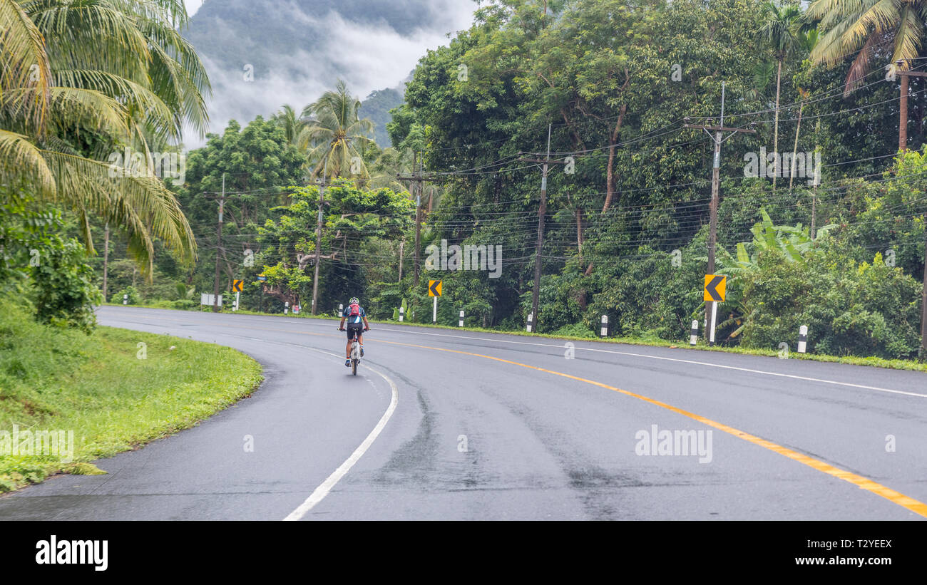 Männliche Radfahrer reiten Fahrrad auf der Autobahn im regen Wald von Kiriwong Stockfoto