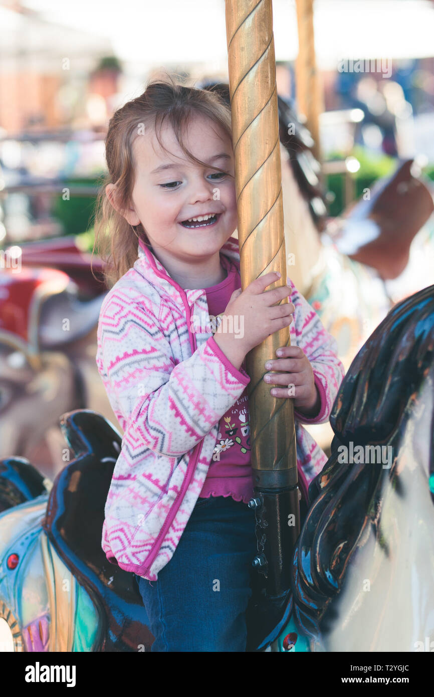 Wenig liebenswert lächelnde Mädchen ein Pferd Reiten am Kreisverkehr Karussell an Kirmes Stockfoto