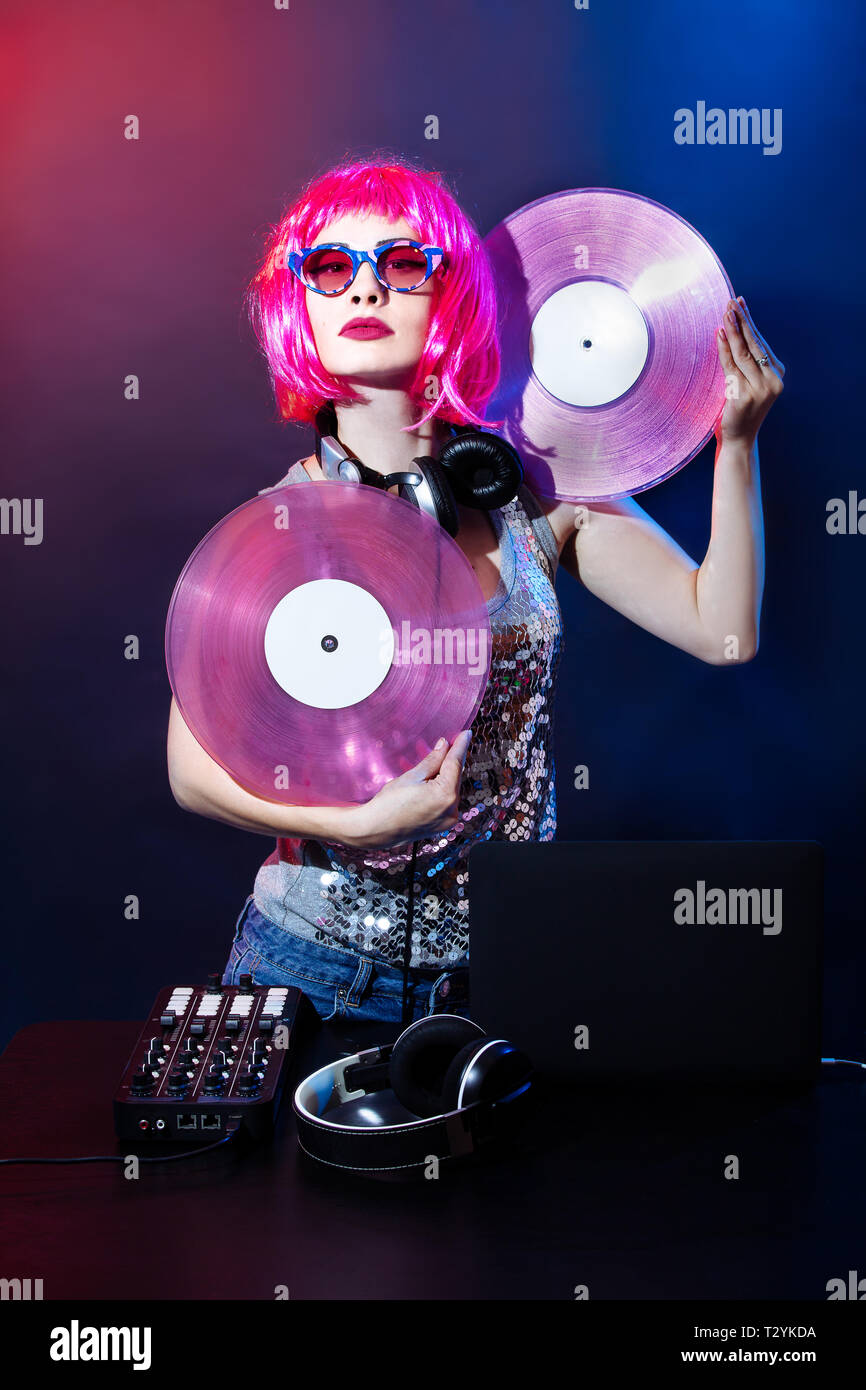 Porträt einer jungen Frau mit rosa Haaren und vintage Brille auf roten und blauen Hintergrund. DJ-Frau mit headphne und rosa Vinyls spielt Musik Disko. Gla Stockfoto