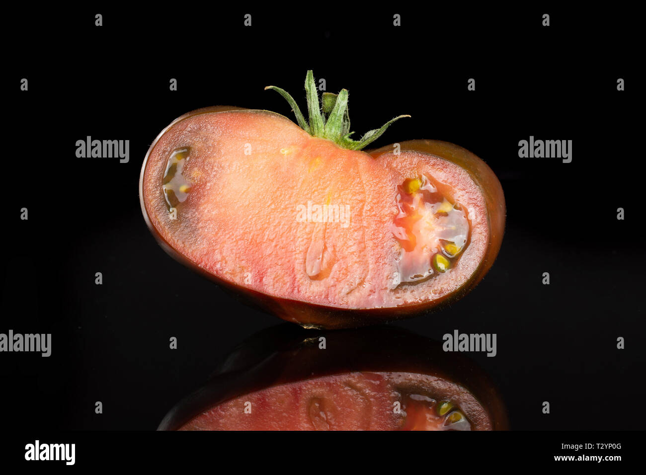 Die Hälfte der frischen Tomate primora auf schwarzem Glas isoliert Stockfoto
