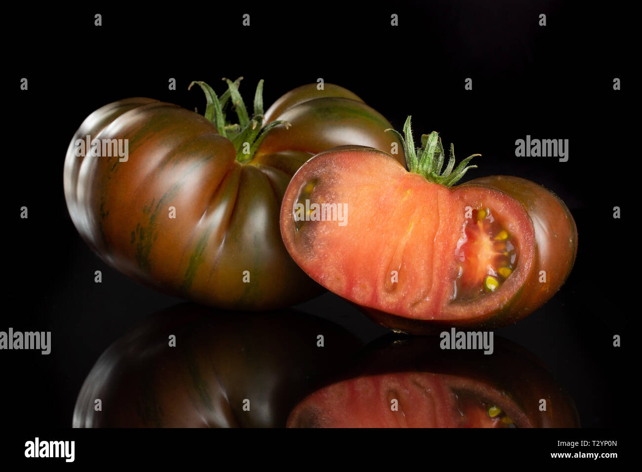 Gruppe von einer ganzen Hälfte der frischen Tomate primora auf schwarzem Glas isoliert Stockfoto