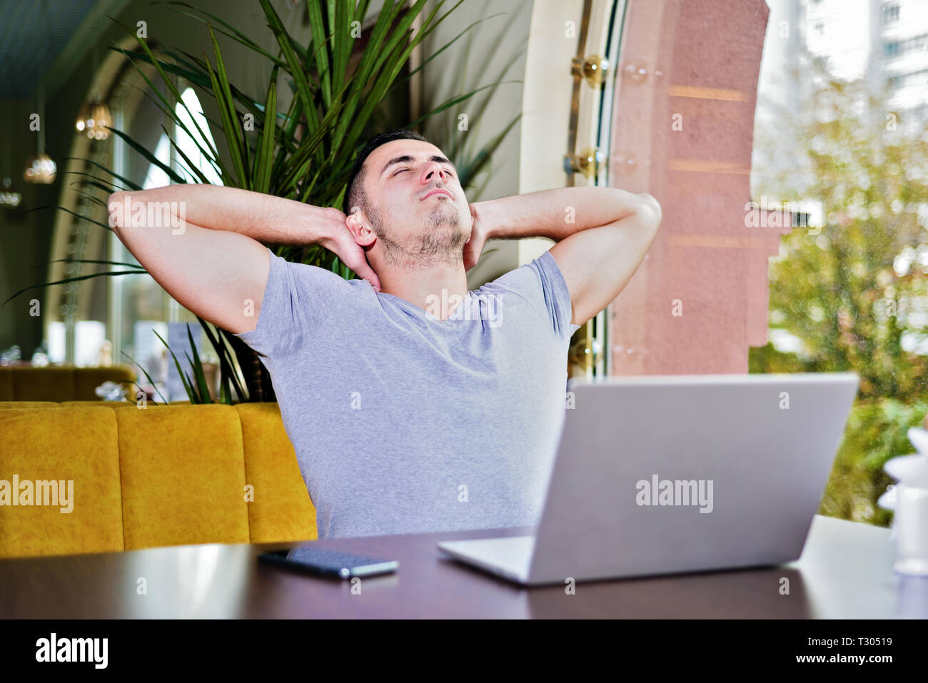 Mann mit Laptop im Cafe entspannt. Ein junger Kerl mit zwei Händen halten Position und ruht aus. Stockfoto