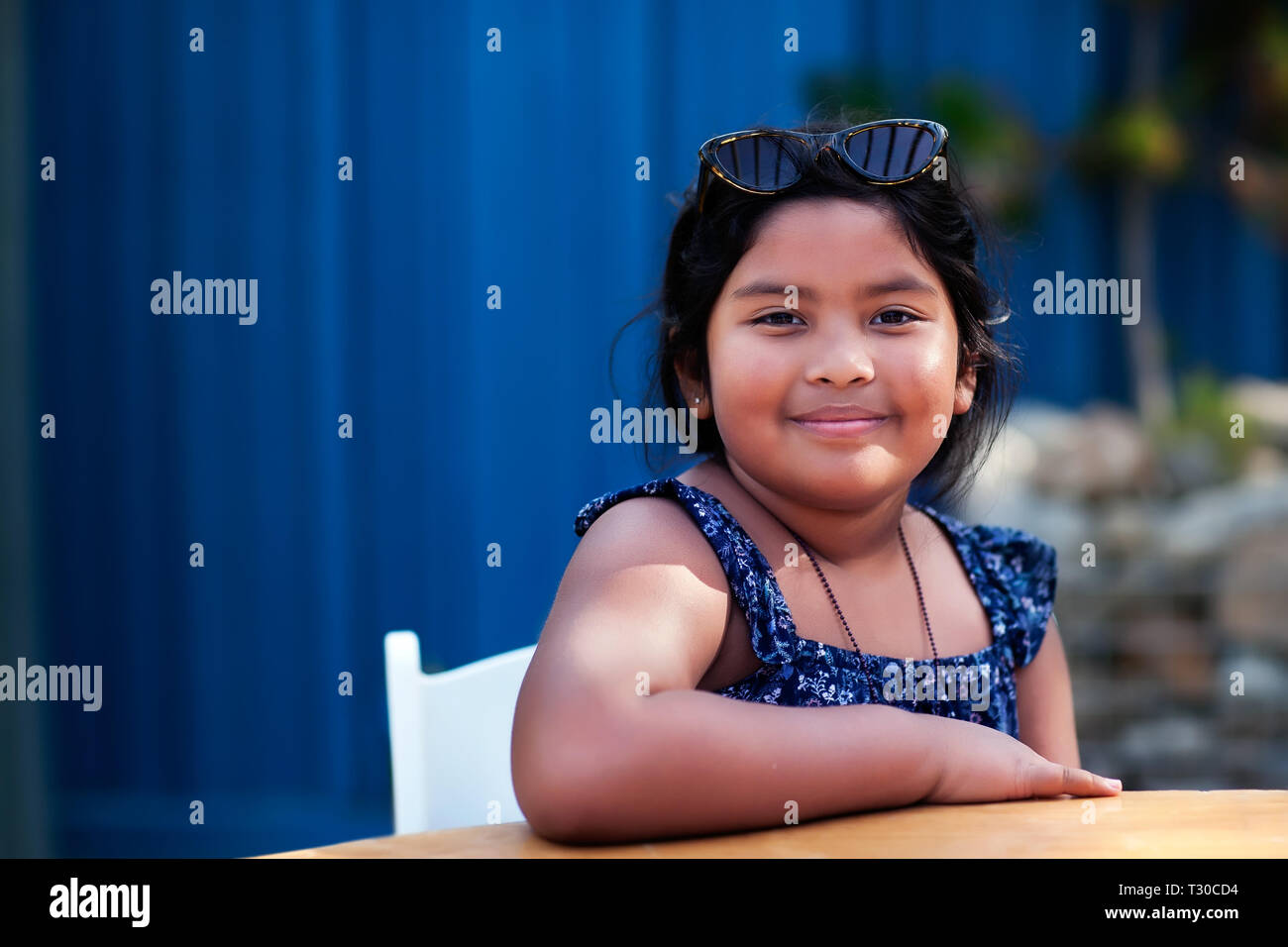 Porträt einer freundlichen kleinen Mädchen mit Schattierungen und bescheidene Kleidung beim Sitzen und Lächeln in einem Außenbereich. Stockfoto