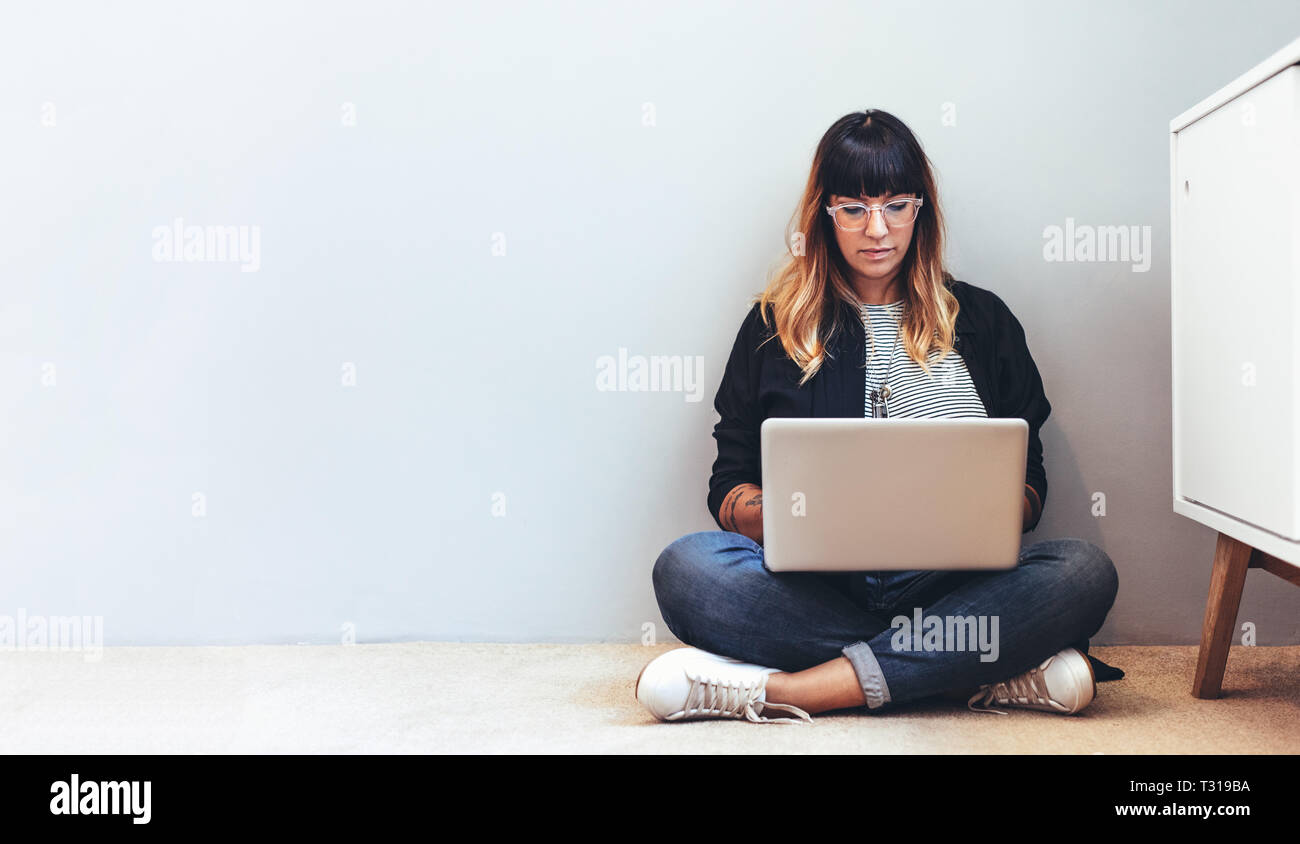 Weibliche Freiberufler arbeiten am Laptop sitzen auf dem Boden. Frau mit einem Laptop von zu Hause aus arbeiten. Stockfoto