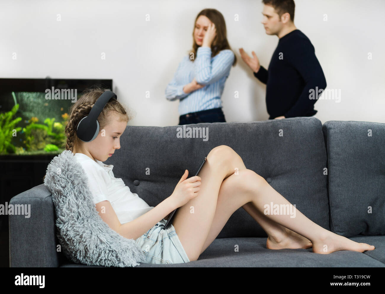 Kleine Mädchen in den Kopfhörern über Tablet-PC, während ihre Eltern im Hintergrund Streit. Stockfoto