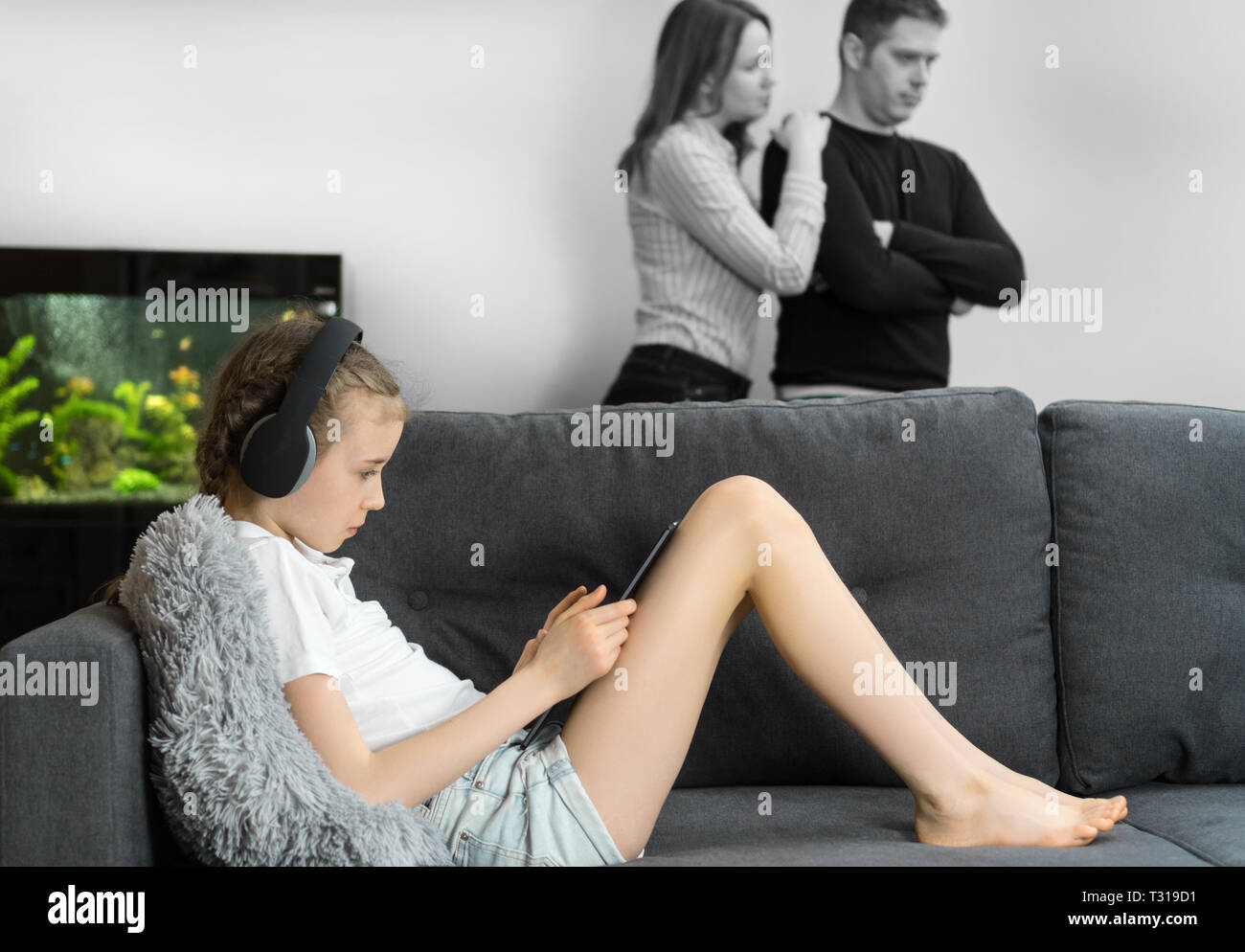 Kleine Mädchen in den Kopfhörern über Tablet-PC, während ihre Eltern im Hintergrund Streit. Stockfoto