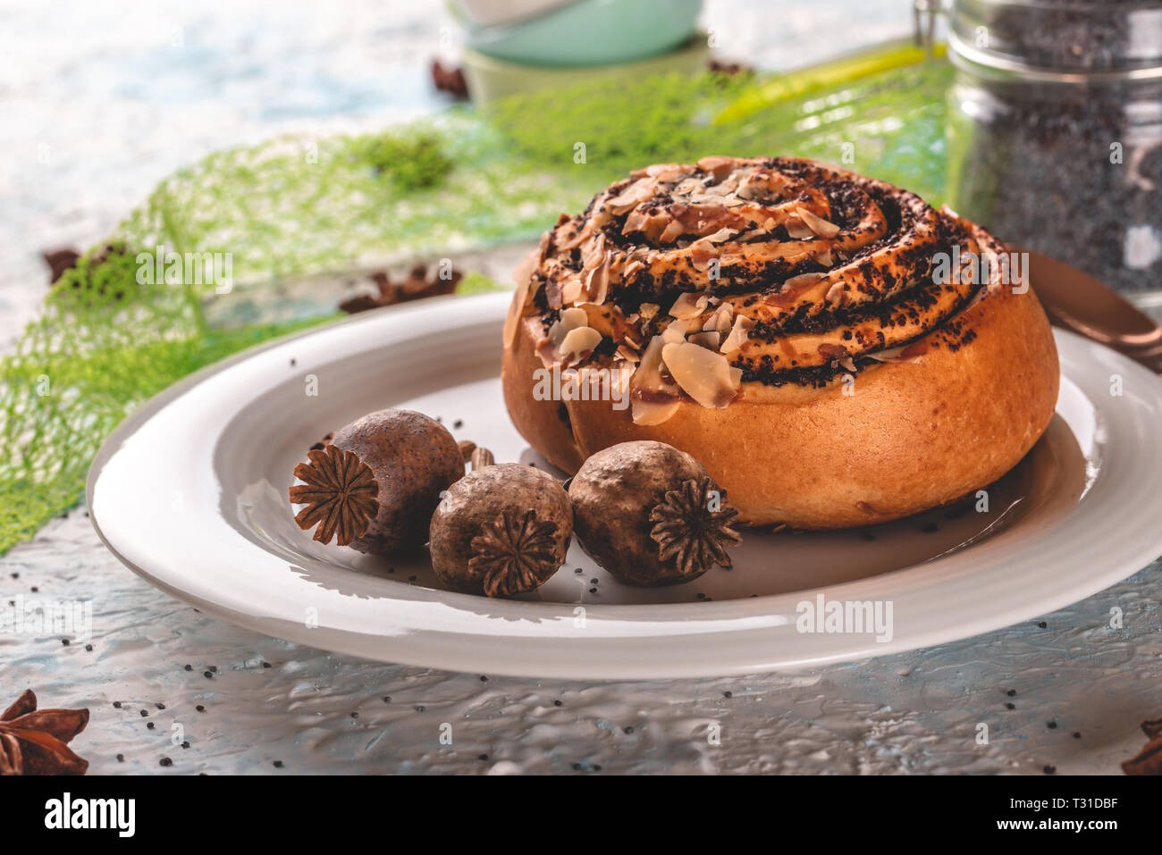 Horizontale Foto der süßen gerollte Brötchen gefüllt mit Mohn. Bun ist auf weiße Platte mit wenigen poppyheads. Glas gar mit Mohn und gestapelte kleine Schalen ein Stockfoto