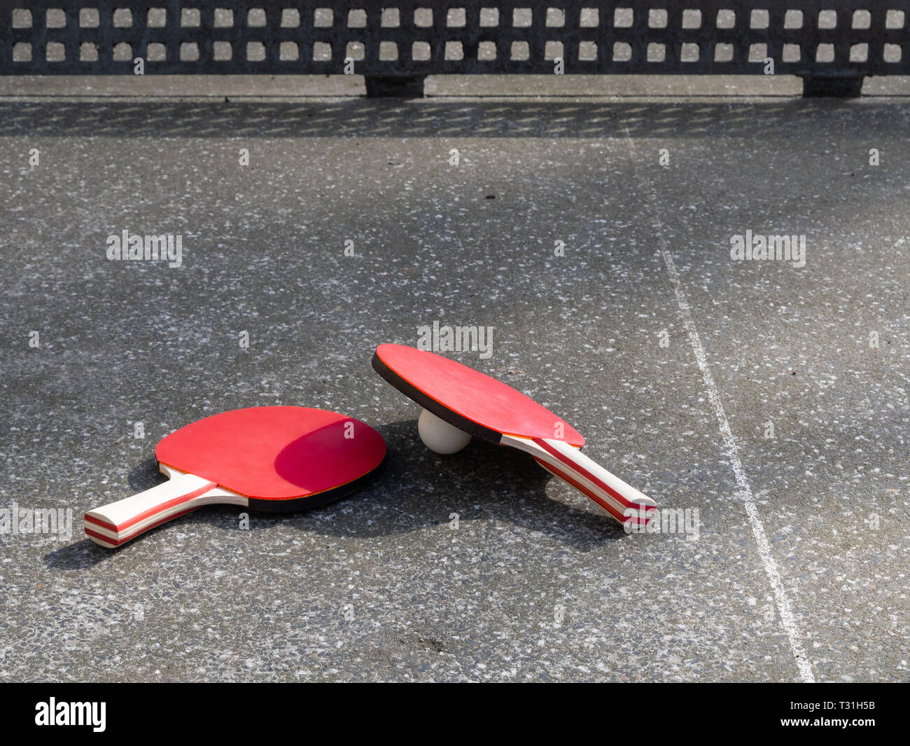 Zwei Tischtennisschläger liegen auf einem Beton Tischtennisplatte. Spielplatz Objekt, Tageslicht. Aktiv im Freien. Stockfoto