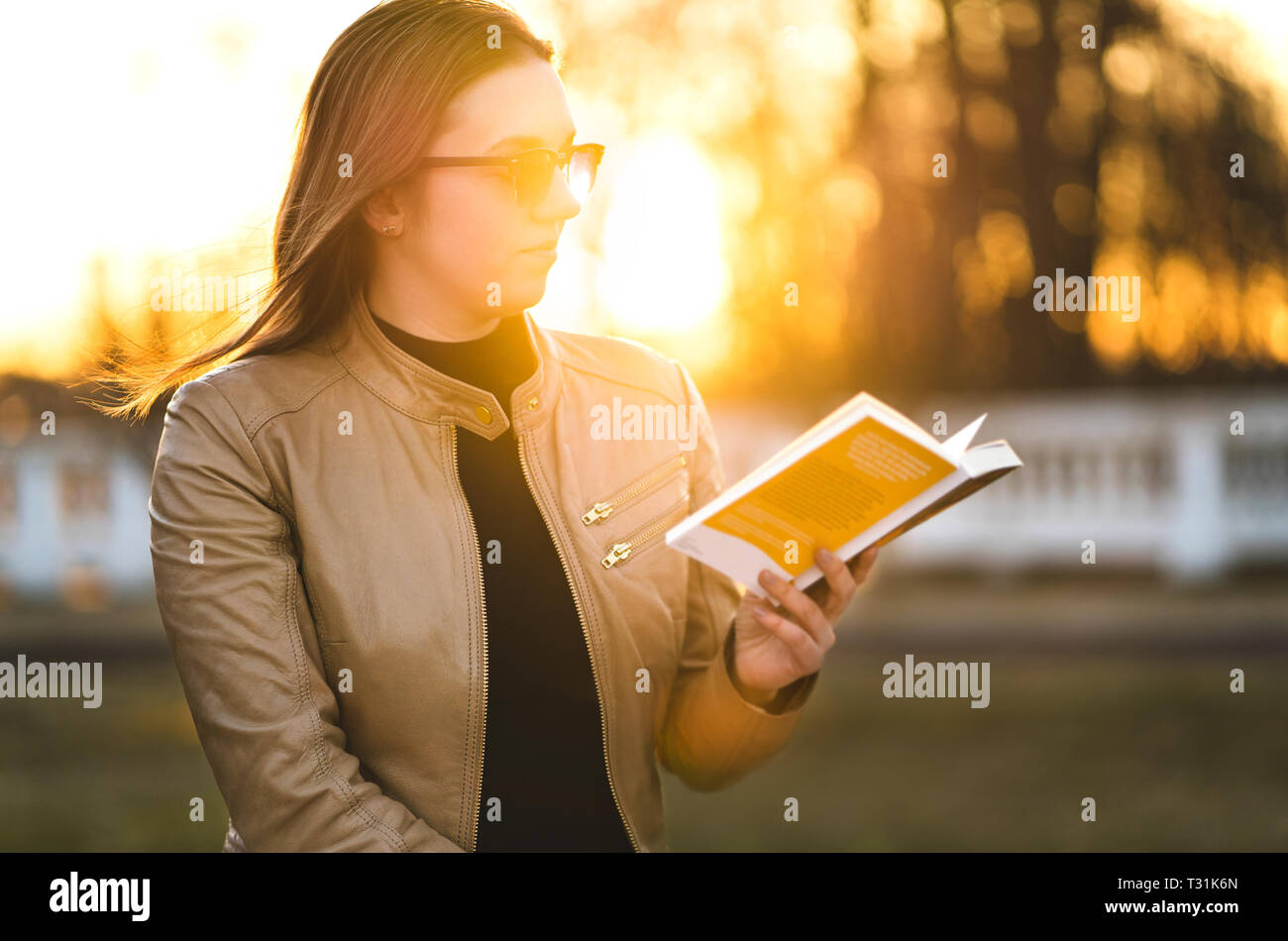Frau liest Buch draußen im Park. Dame genießen Roman draußen in den Sonnenuntergang am Abend. Studenten studieren. Stockfoto