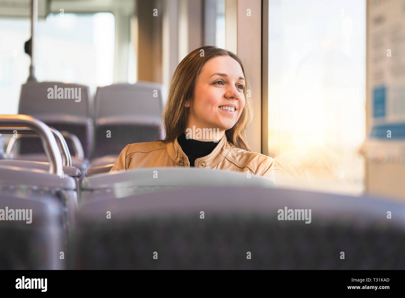 Fröhliche Dame, die in Bus, Bahn, Straßenbahn oder U-Bahn auf das Fenster blickt. Lächelnde Frau, die mit öffentlichen Verkehrsmitteln unterwegs ist, um zu arbeiten oder Urlaub zu machen. Stockfoto