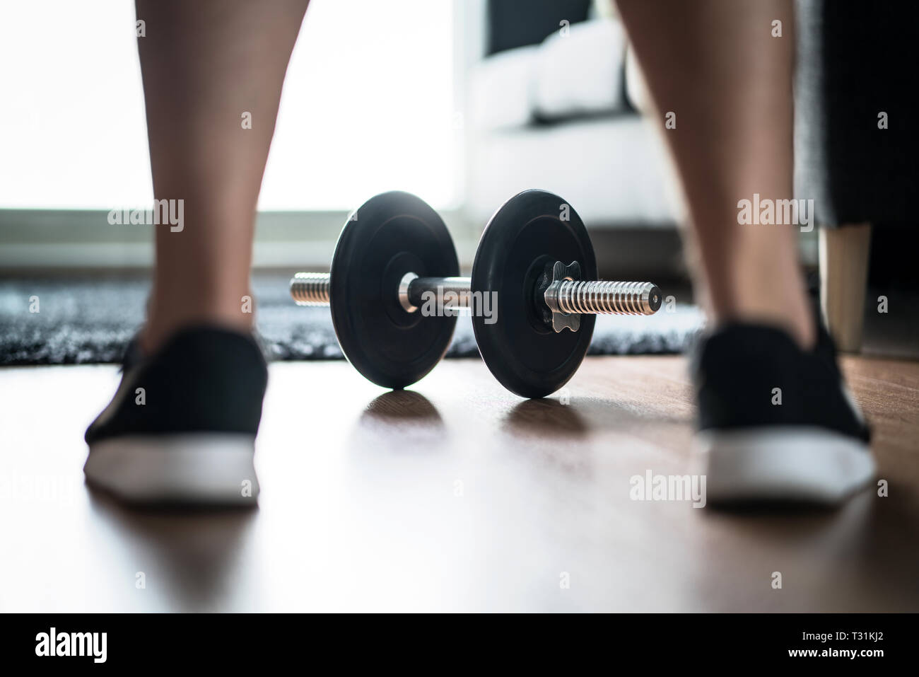 Fitness-Motivation, Entschlossenheit und Herausforderungskonzept. Mann, der mit dem Training und der Bewegung beginnt. Muskeltraining in der Heimturnhalle. Hanteln zwischen den Turnschuhen. Stockfoto