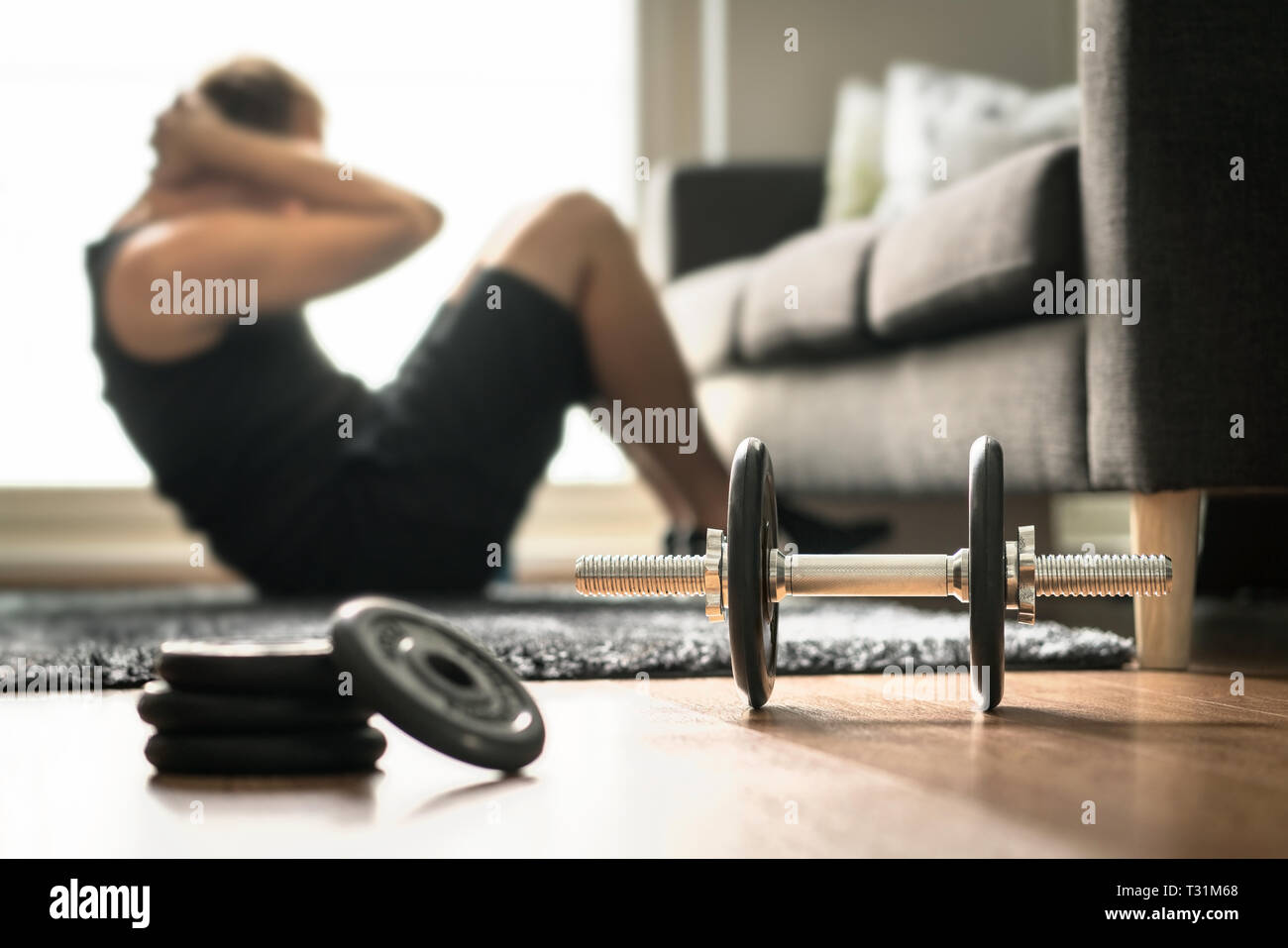 Heimtraining. Der Mann trainiert und knirschen im Fitnessstudio im Wohnzimmer. Kerl, der Sit ups macht. Vor dem Krafttraining aufwärmen. Fitnesskonzept mit Hanteln. Stockfoto