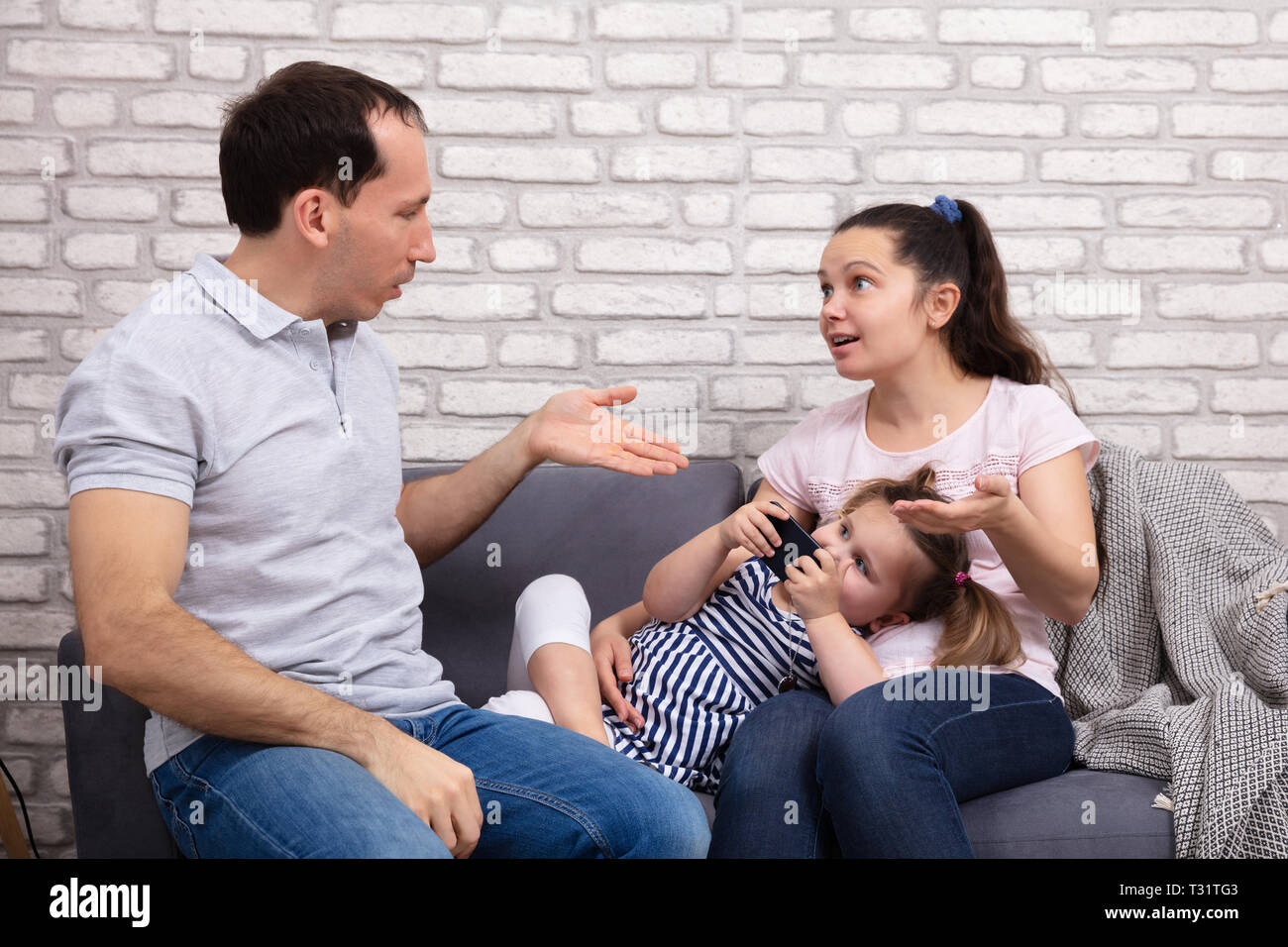 Paar Argumentieren zu Hause, während ihre Tochter nach Mobilephone Sitzen auf einem Sofa Stockfoto