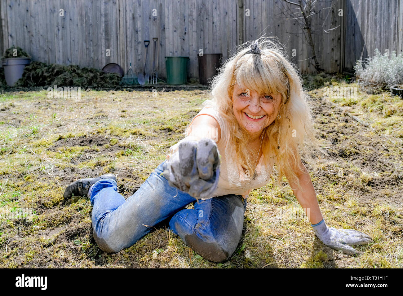 Blonde Frau mittleren Alters mit Schmutz auf Ihrem Gesicht, Arbeiten in Ihrem Garten. Siehe Alamy Bild W3RBAY für daraus resultierende Wildblumen. Stockfoto