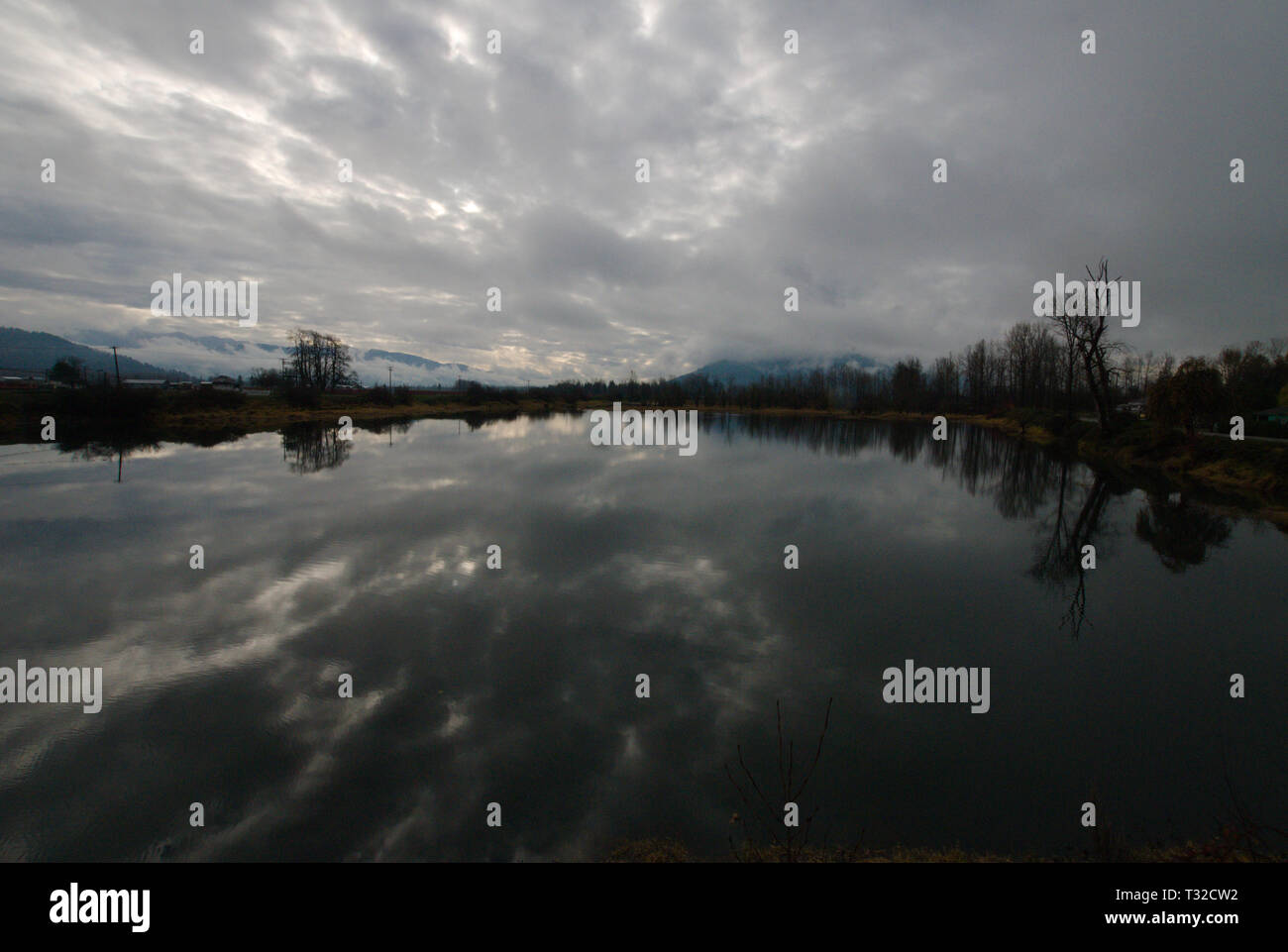 Am ruhigen Ufer des Vedder River spiegelt sich ein turbulenter grauer, bedeckter Himmel in Chilliwack, British Columbia, Kanada, wider Stockfoto