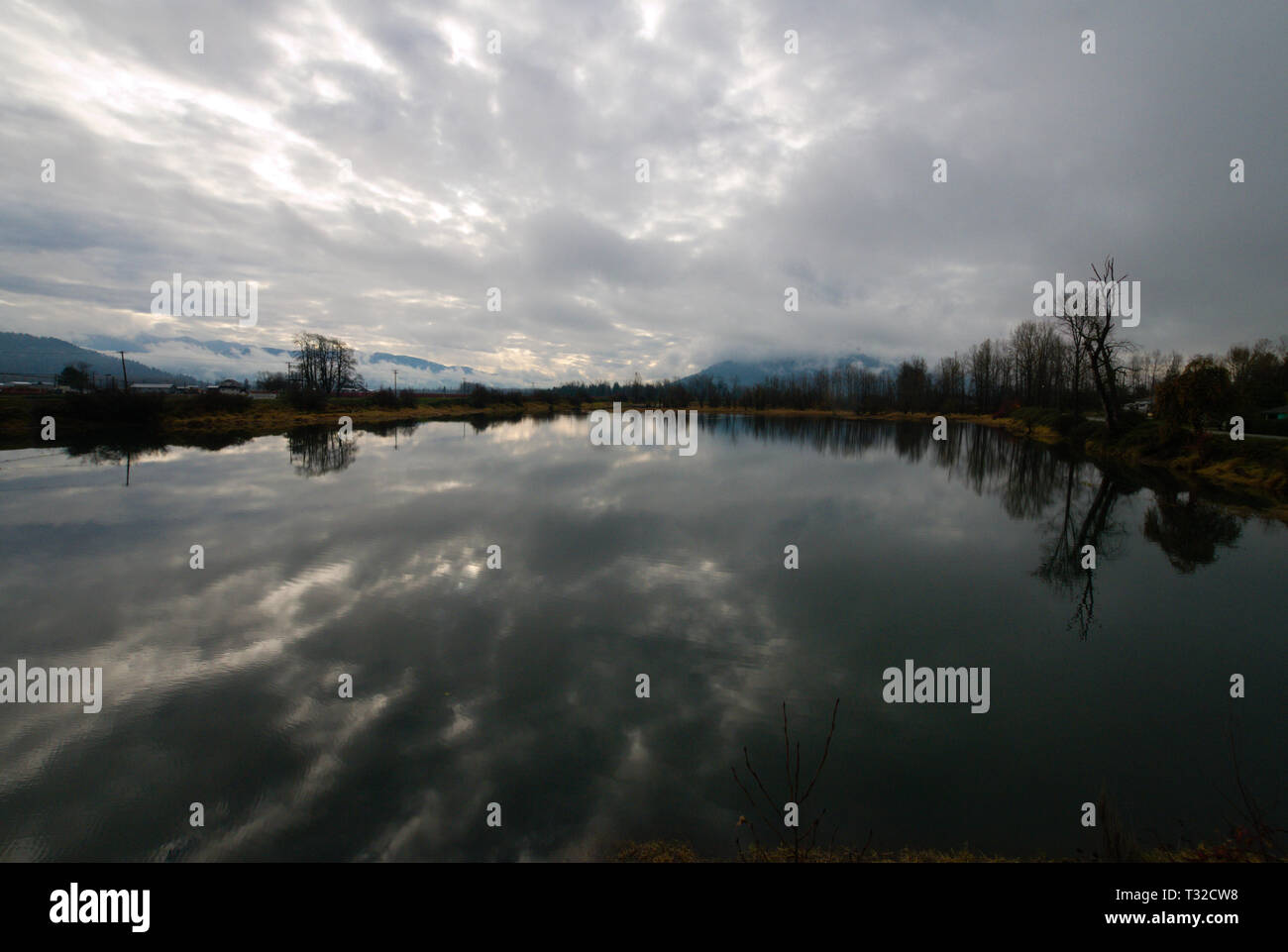 Am ruhigen Ufer des Vedder River spiegelt sich ein turbulenter grauer, bedeckter Himmel in Chilliwack, British Columbia, Kanada, wider Stockfoto