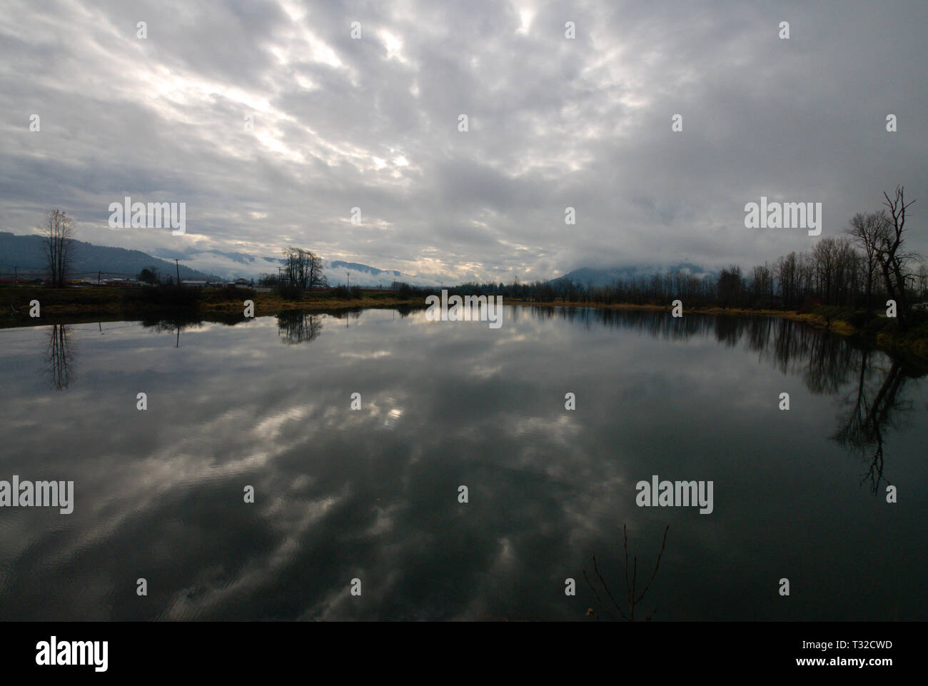 Am ruhigen Ufer des Vedder River spiegelt sich ein turbulenter grauer, bedeckter Himmel in Chilliwack, British Columbia, Kanada, wider Stockfoto