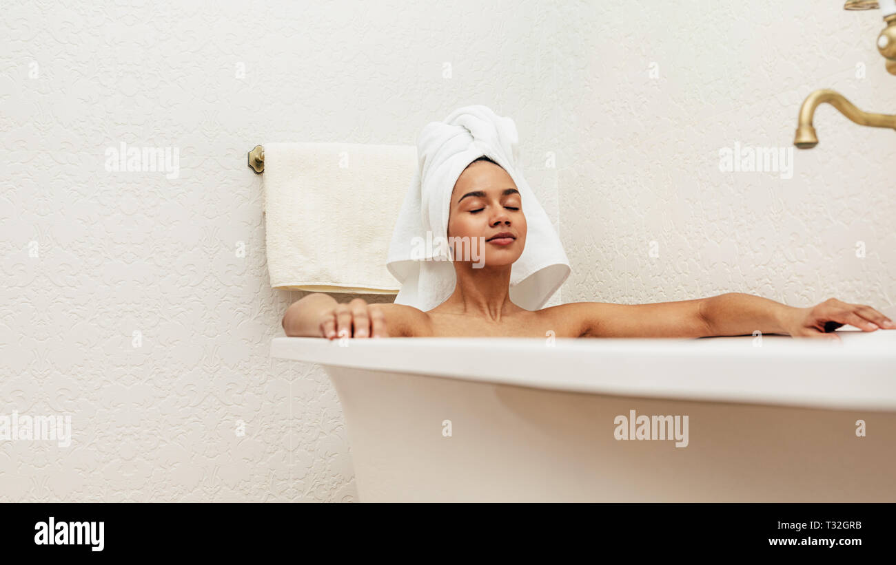 Frau mit weißen Handtuch auf dem Kopf entspannen in der Badewanne mit geschlossenen Augen Stockfoto