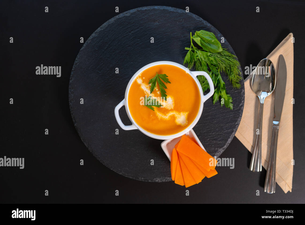 Schüssel leckere hausgemachte heiße Kürbissuppe mit passenden orange Serviette serviert in einer weißen Schüssel auf einem dunklen Hintergrund mit Utensilien und Platz kopieren Stockfoto