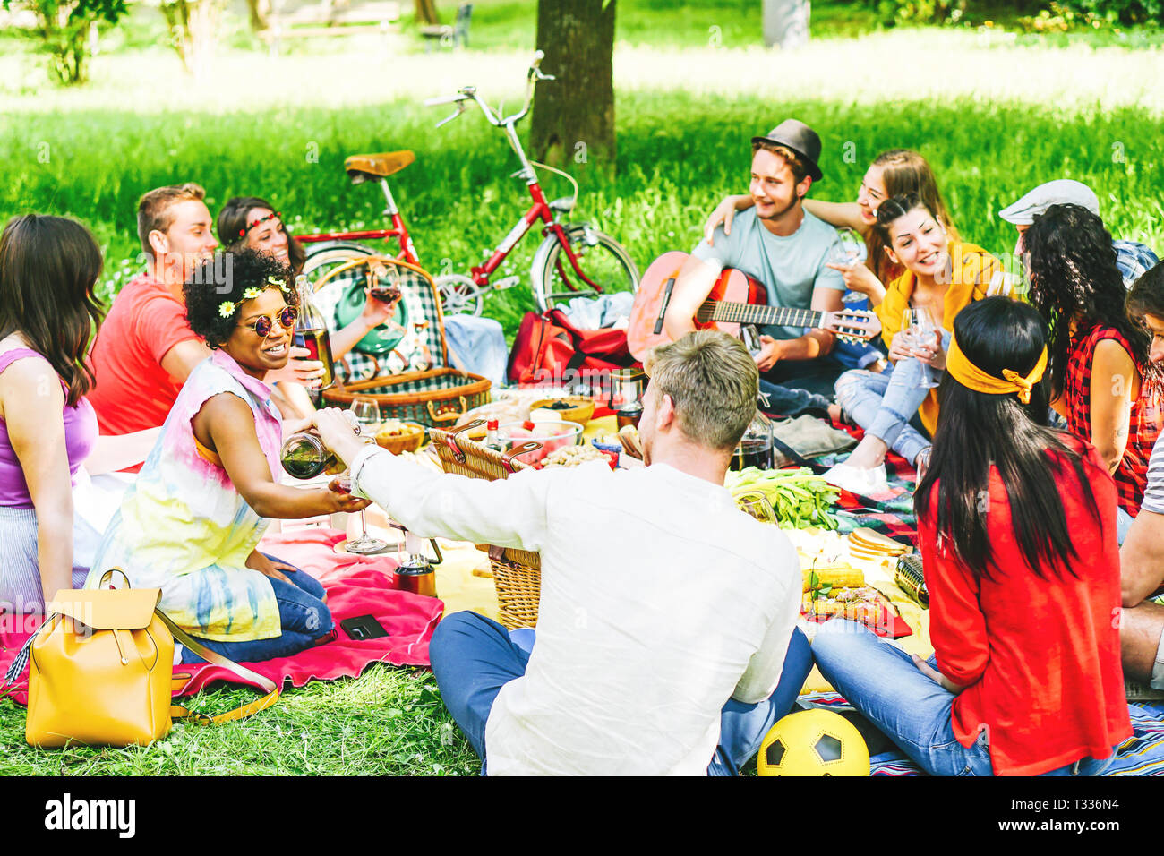 Eine Gruppe von Freunden ein Picknick genießen, beim Essen und Trinken Rotwein sitzen auf Decke in einem Park im Freien - junge Menschen, die eine lustige Begegnung Stockfoto