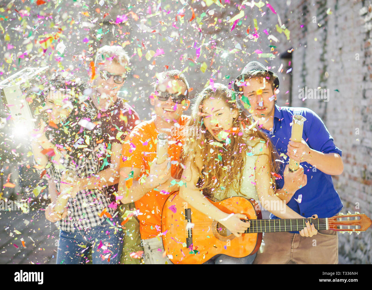 Junge Freunde ein großes Straßenfest - Gruppe von glücklichen Menschen werfen von Konfetti in, Gitarre spielen, Singen und Tanzen auf der Straße Stockfoto