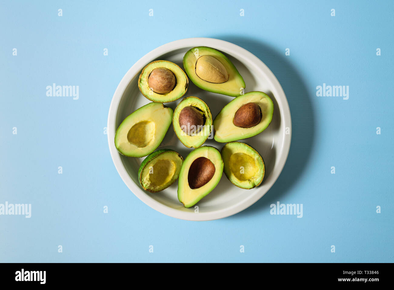 Avocado zur Hälfte auf Keramikplatte. Pastellfarben hellblau hinterlegt. Text Raum Stockfoto