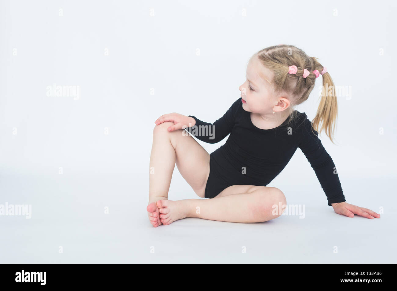 Süße kleine Mädchen in schönen schwarzen Kleid auf dem Boden sitzend auf weißem Hintergrund Stockfoto