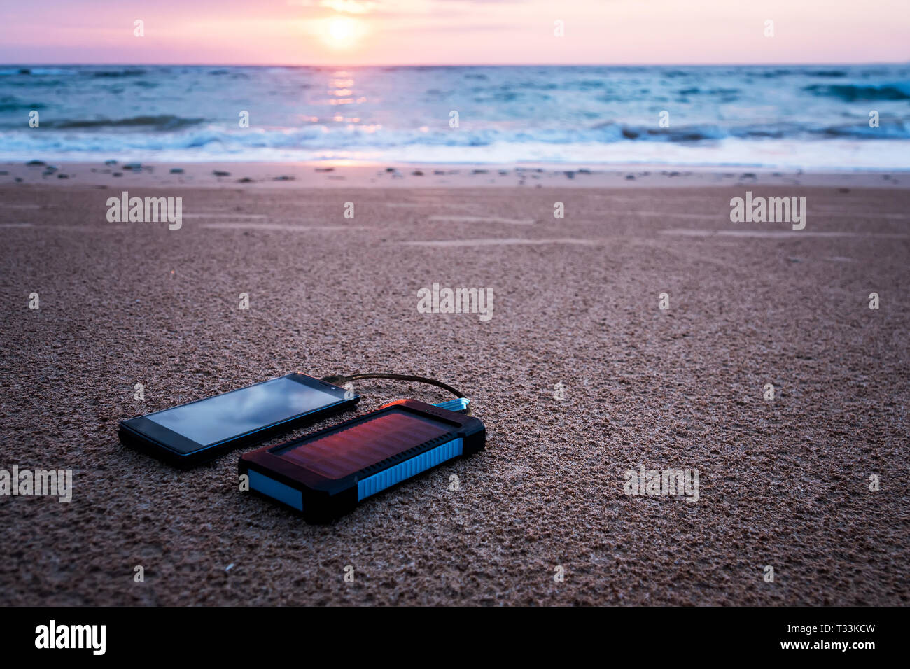 Akku Solar Energy Device auf einem Hintergrund der Sandstrand von einer unbewohnten Insel. Smart Phone aus der Solar Batterie aufladen. schönen tropischen Stockfoto