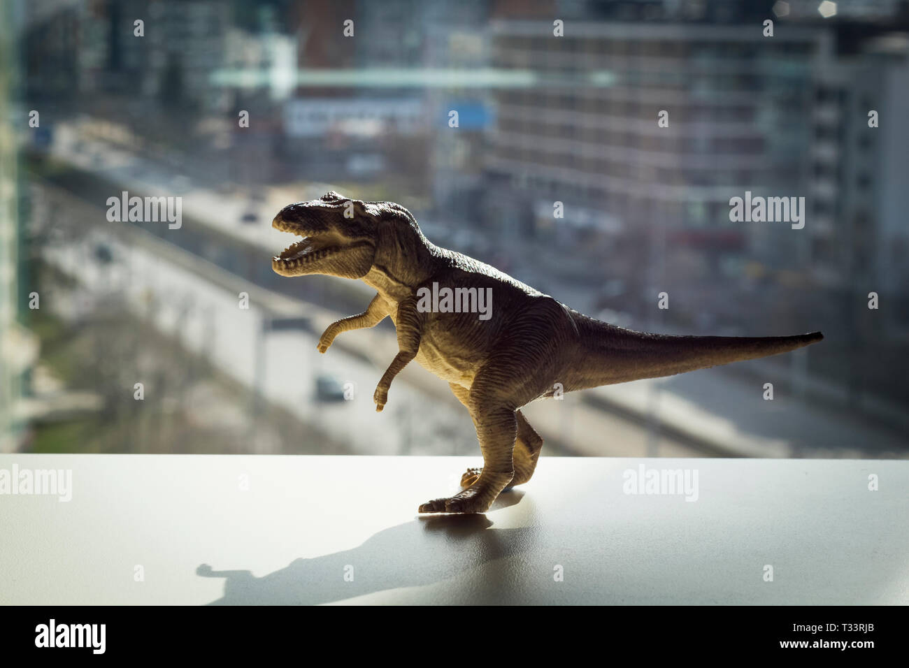 T-Rex Dinosaurier Spielzeug mit einer unscharfen Stadt hinter Stockfoto