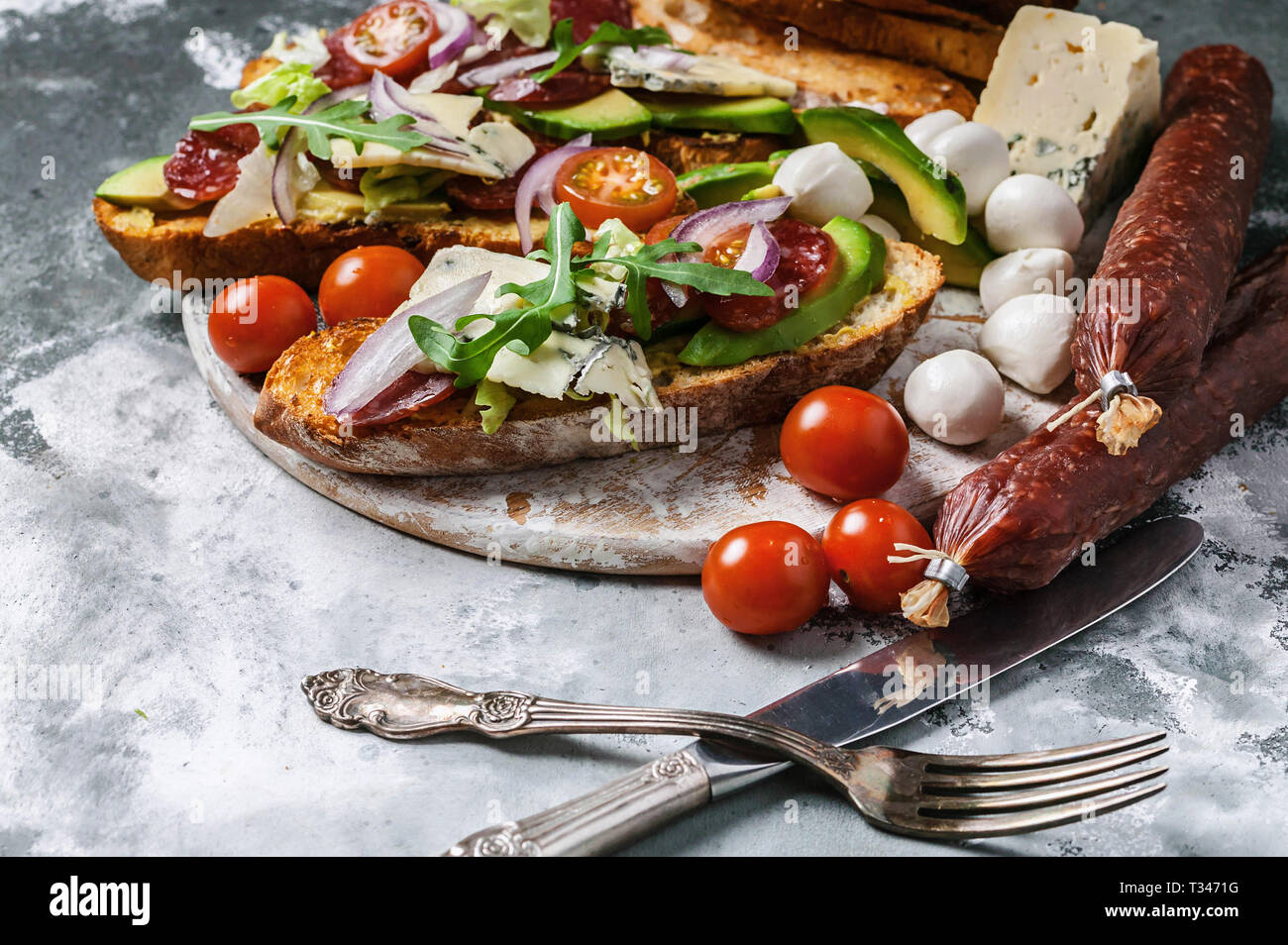 Köstliche Sandwiches mit geräucherter Wurst, Avocado, Käse, Tomaten, roten Zwiebeln und Rucola. Stockfoto