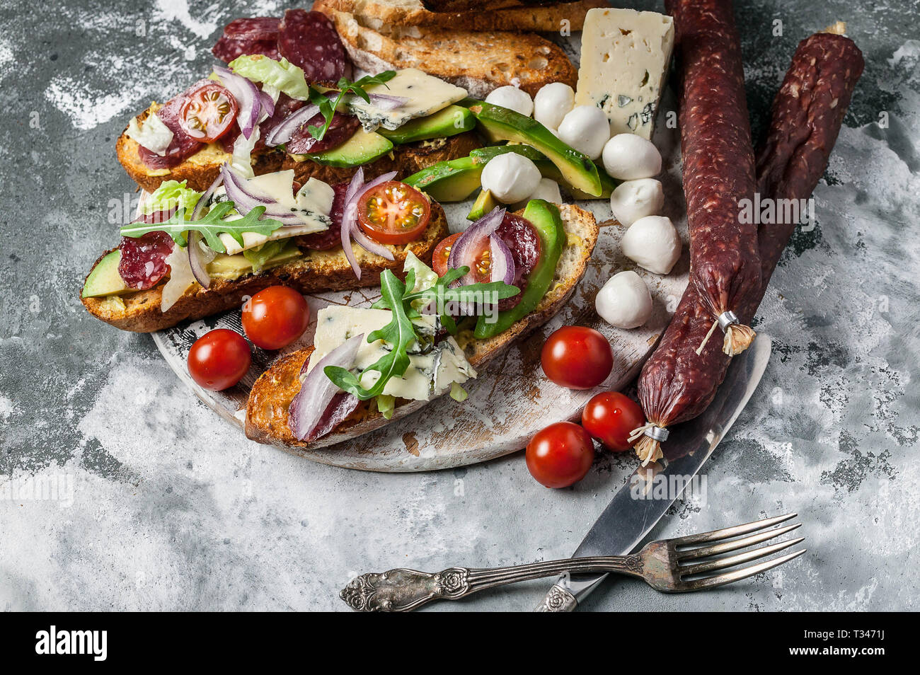 Köstliche Sandwiches mit geräucherter Wurst, Avocado, Käse, Tomaten, roten Zwiebeln und Rucola. Stockfoto