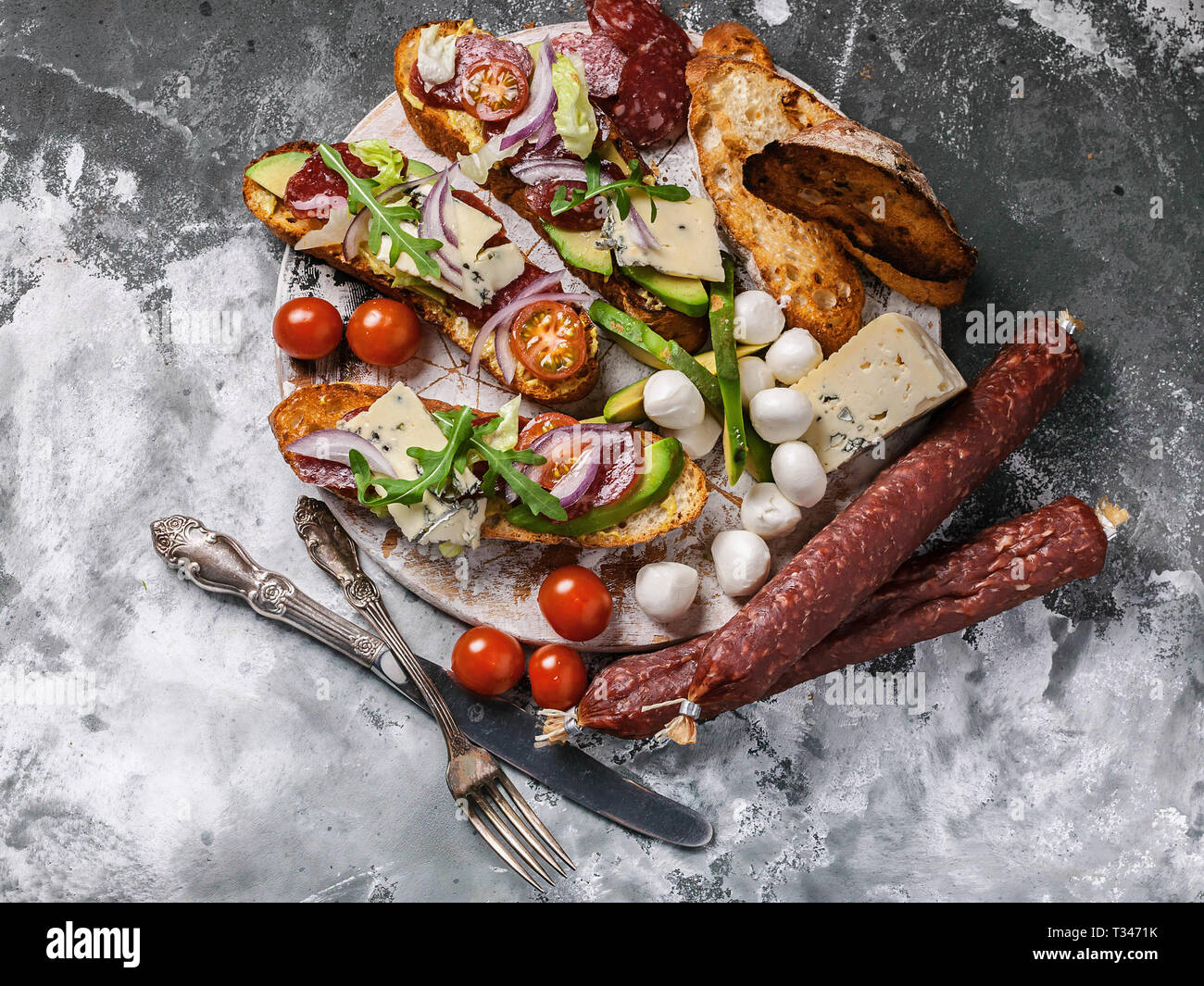 Köstliche Sandwiches mit geräucherter Wurst, Avocado, Käse, Tomaten, roten Zwiebeln und Rucola. Ansicht von oben Stockfoto