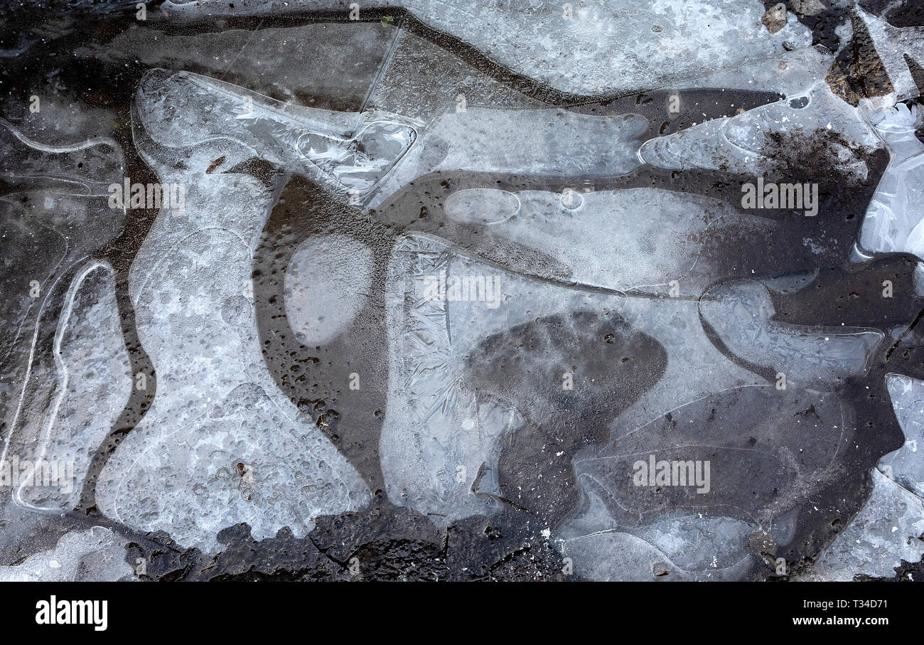Eisschicht auf einem strassenrand Pfütze mit Luft unter gefangen. Stockfoto