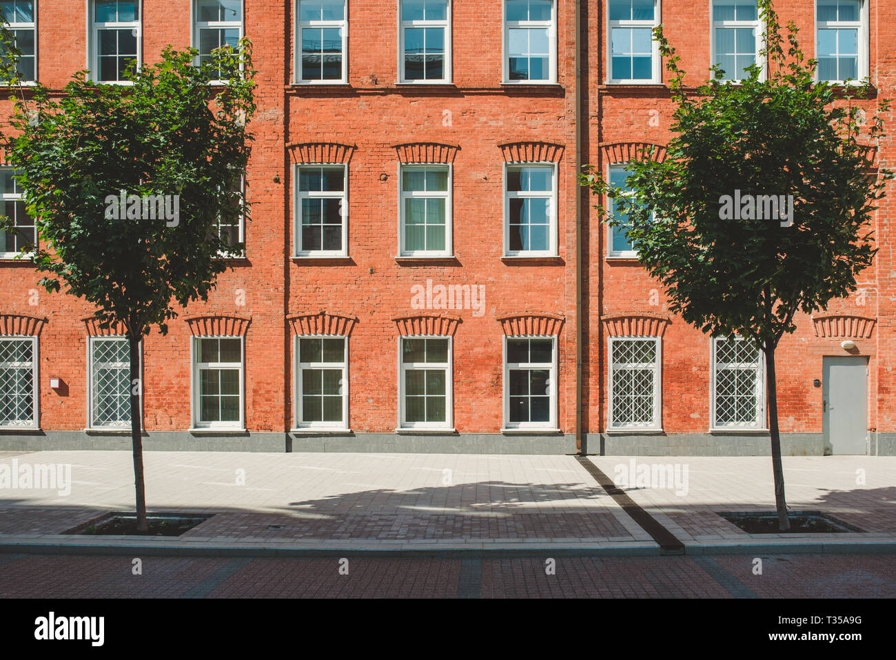 Bürogebäude im Loft-Stil. Große Fenster. Red brick wall. Grüne Büsche auf der Mitte. Flache Fassade Zusammensetzung Stockfoto