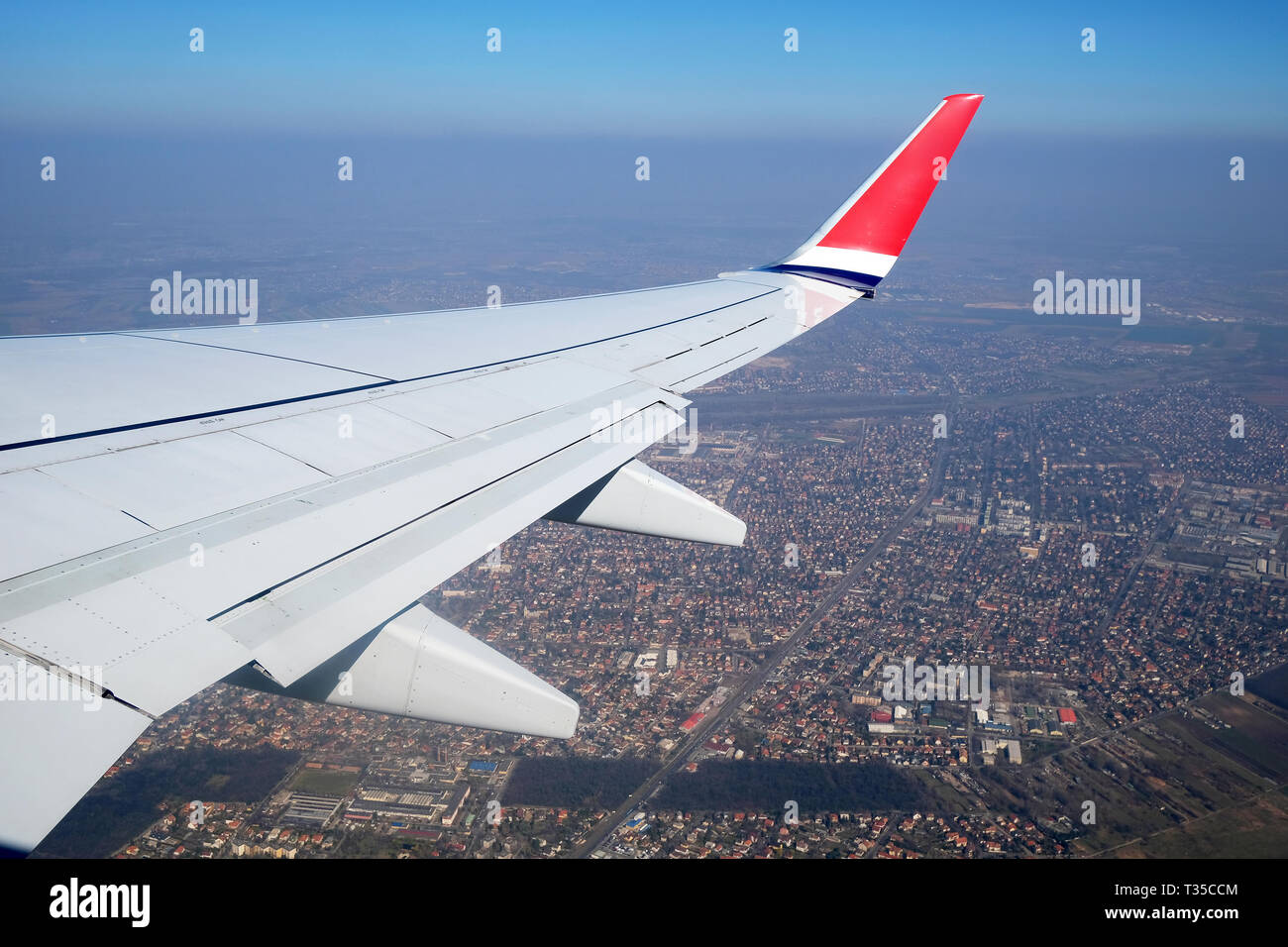 Flügel eines Flugzeugs über Dörfer oder die Landschaft fliegen. Der ebene Tragfläche auf den blauen Himmel und Erde Hintergrund Stockfoto