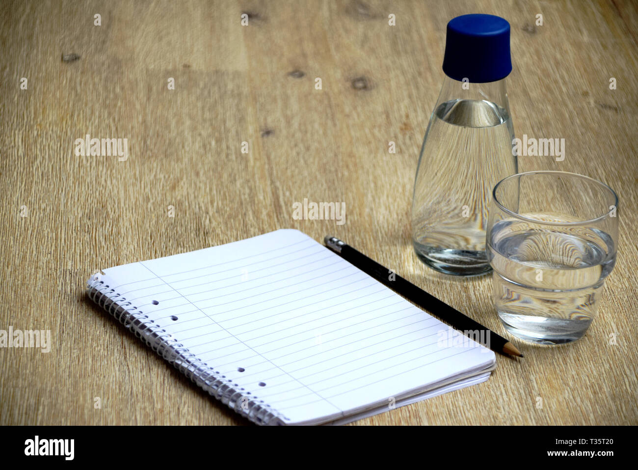 Wasser, Notizbuch und Stift auf hölzernen Tisch Stockfoto