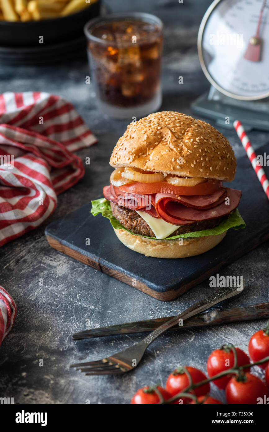 Vorderansicht des leckeren Burger und ein Glas kühlen Soda Drink auf Schwarzes Brett Kartoffeln und Pommes frites auf dem Hintergrund, auf grau Tisch Stockfoto