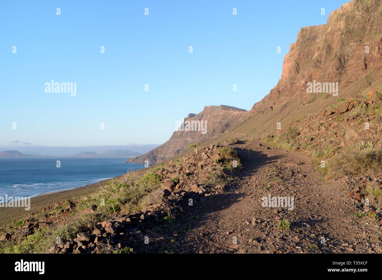 Grobe track und Fußweg entlang der Seite des Famara Klippen, mit im Hintergrund die Insel La Graciosa, Lanzarote, Kanarische Inseln, Februar. Stockfoto