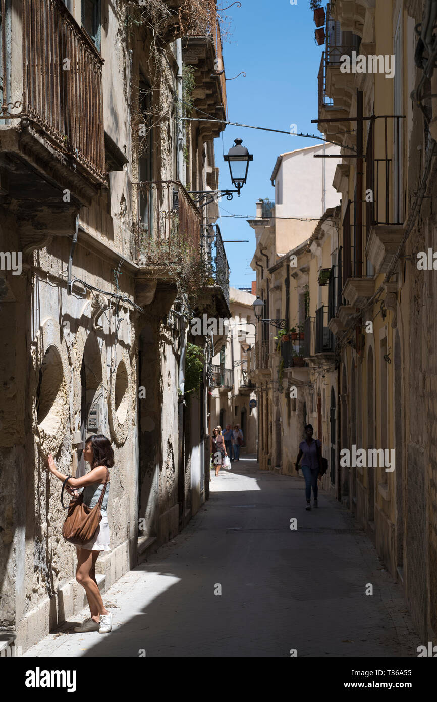 Street Scene Frau rührende alte Stein in reich verzierten Gasse über Dione in Ortigia, Syrakus, Sizilien Stockfoto
