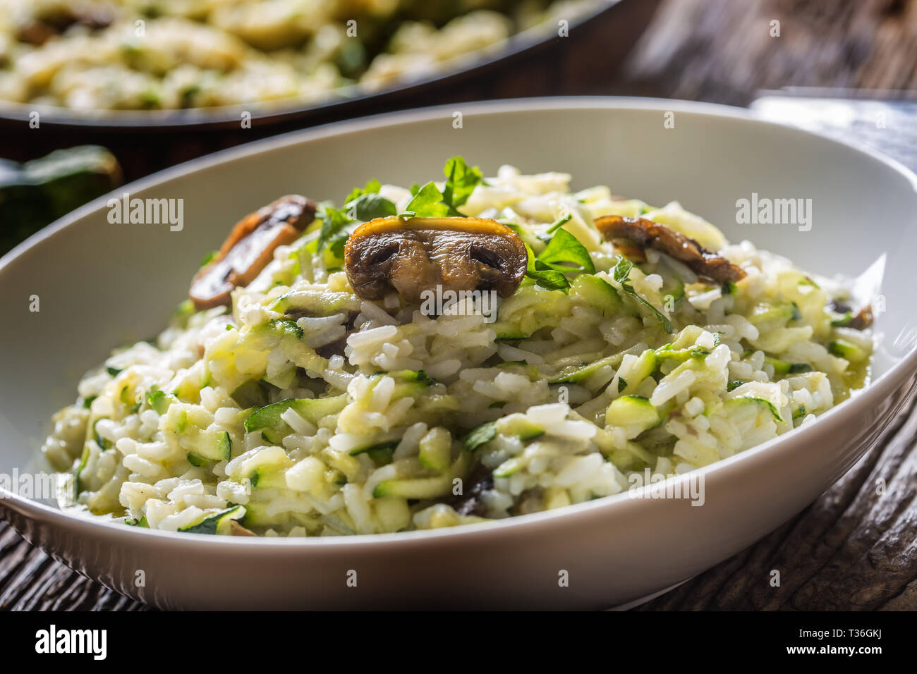 Italienische Risotto mit Zucchini Champignons und Parmesan in weiße Platte. Stockfoto