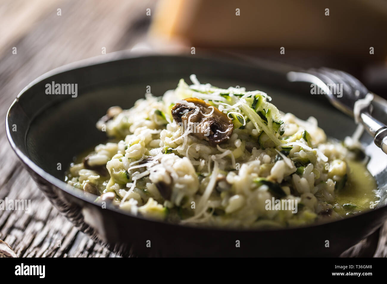 Italienische Risotto mit Zucchini Champignons und Parmesan in dunklen Platte. Stockfoto