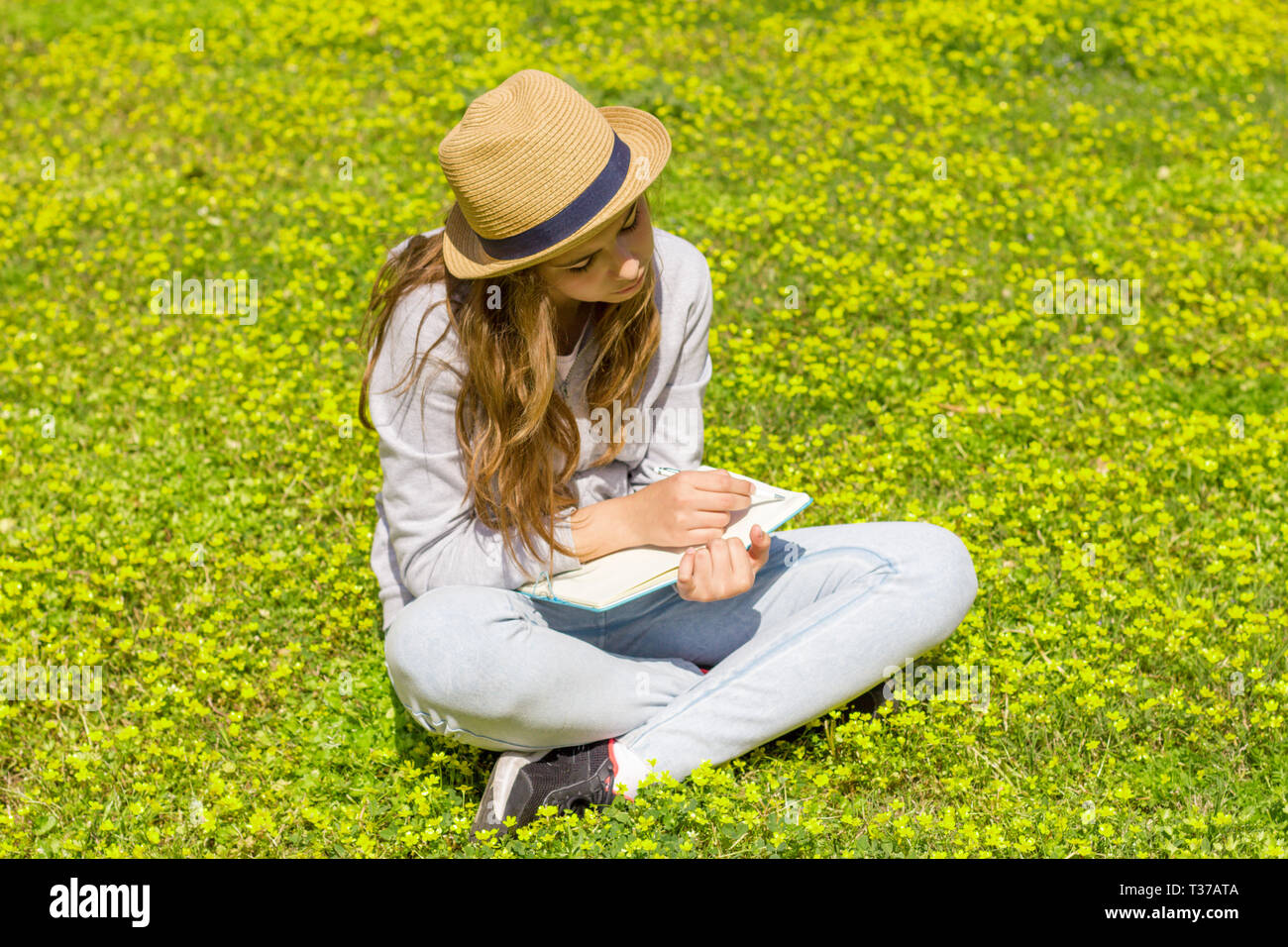 Cute Teen Girl schreibt Notizen auf einem Papierblock auf der grünen Wiese Stockfoto