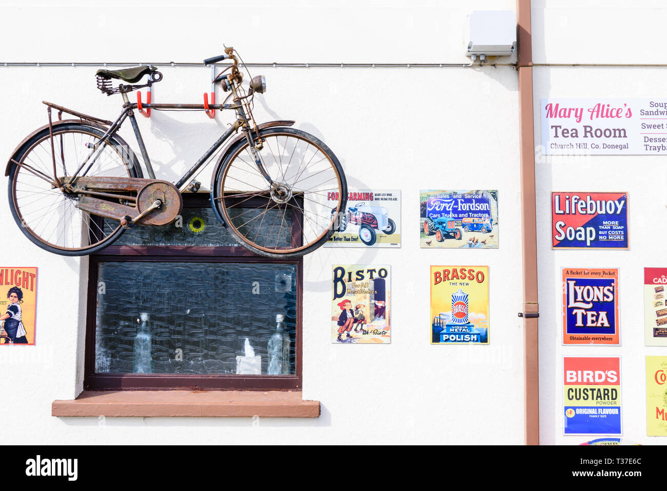 Ein Fahrrad- und ein altmodisches Metall werbeschilder an der Wand außerhalb eines Irish Shop. Stockfoto