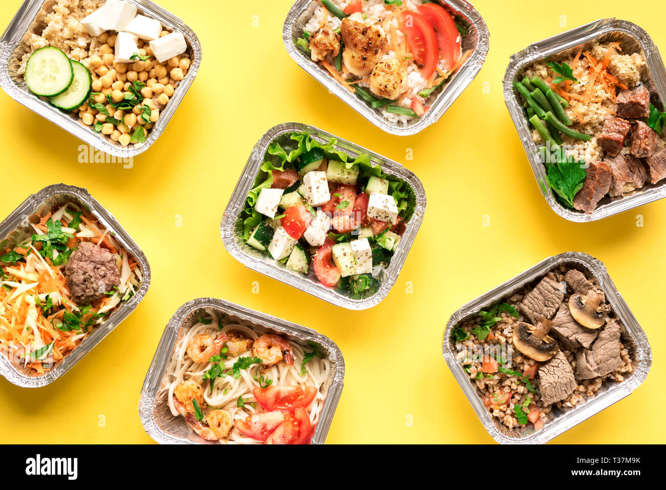 Täglichen Mahlzeiten in Folie Kästen auf gelben Hintergrund, Ansicht von oben, flach. Gesundes Essen Lieferung Konzept. Fitness Ernährung für Ernährung. Stockfoto