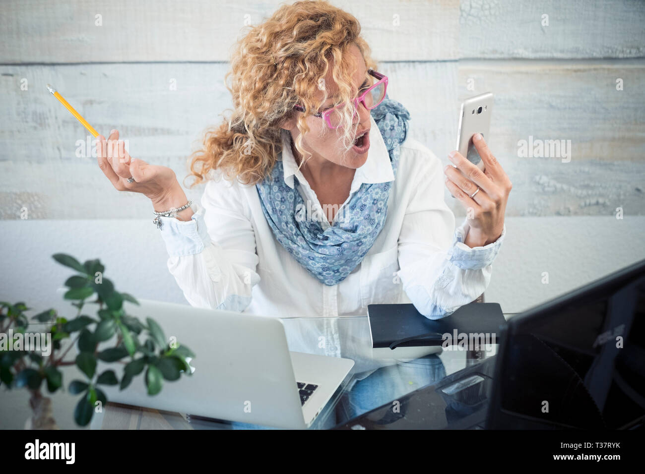 Betonte business Frau schreien beim Anruf - zwei Laptop auf dem Schreibtisch und Technologie überall arbeiten - Workstation mit weiblichen Personen - moderne j Stockfoto
