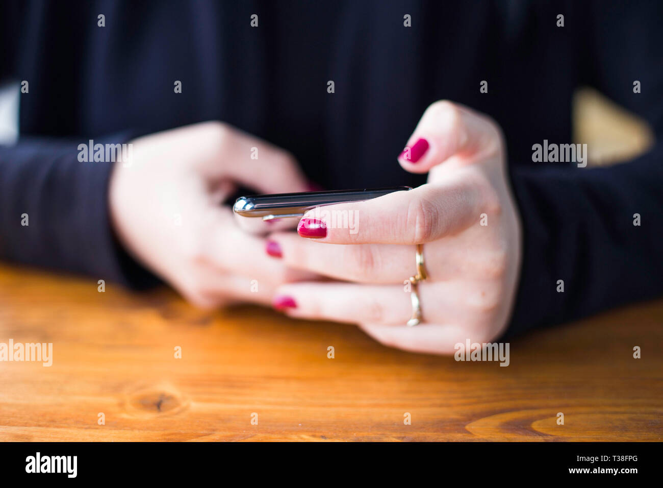 Frau in Schwarz shirt Texteingabe auf Smartphones im Cafe, kein Gesicht, Nahaufnahme, rote Finger, Kommunikationskonzept Stockfoto