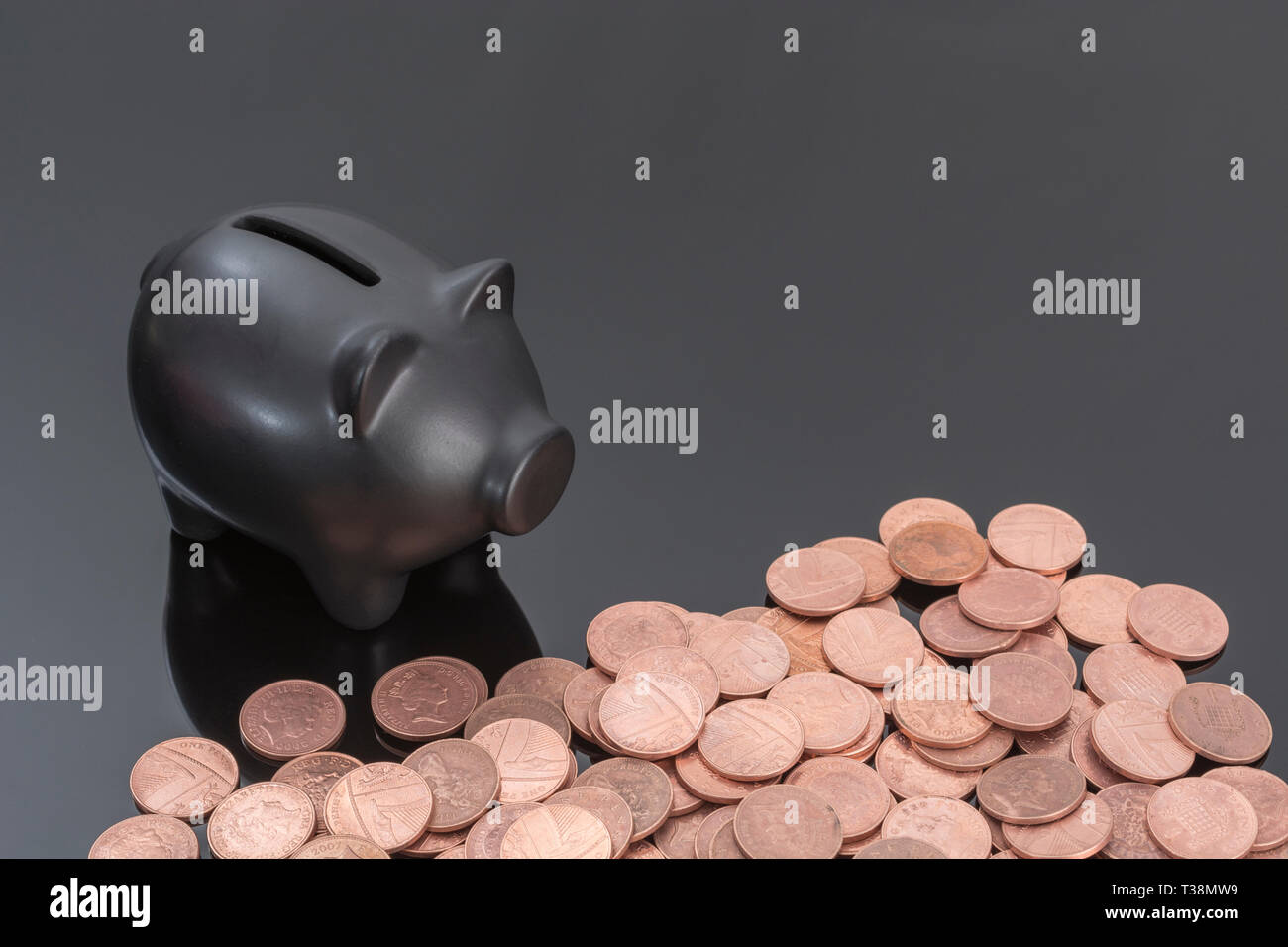 Schwarzer Keramik Sparschwein mit britischen Münzen auf reflektierenden schwarzen Hintergrund. Metapher für Geld sparen, sparen, sparen Pennies, Britische Pennies. Stockfoto